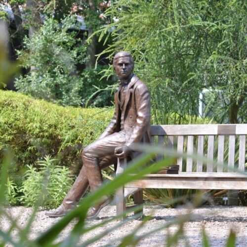 The Darwin Bench in Darwin Garden at Christ’s College, Cambridge, located in a peaceful courtyard garden with trees and planting.