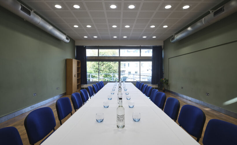 JCR meeting room space at Christ's College, Cambridge set up in a boardroom style with glasses and water and a view of the window. A versatile boardroom space in Cambridge