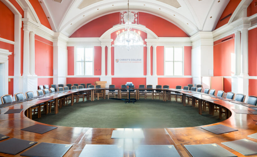 The Plumb Auditorium at Christ’s College, Cambridge, with high ceilings, polished wooden tables and beautiful chandelier lighting. This room is set up in a meeting room style.