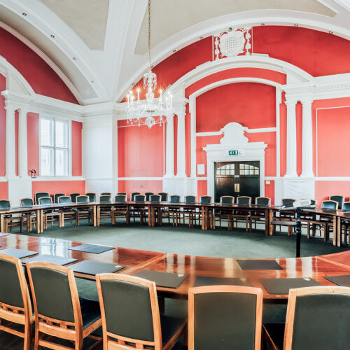 The Plumb Auditorium at Christ’s College, Cambridge, with high ceilings, polished wooden tables and beautiful chandelier lighting. This room is set up in a meeting room style. A great conference space in Cambridge.