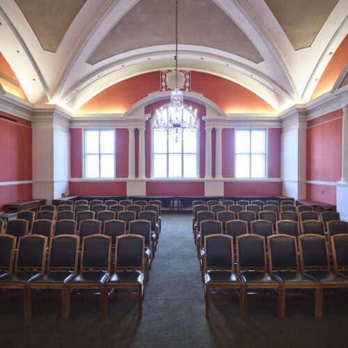 The Plumb Auditorium at Christ’s College, Cambridge, with high ceilings, polished wooden tables and beautiful chandelier lighting. This room is set up in a classroom style.