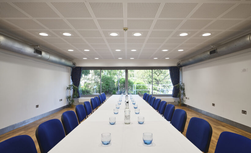 TV Meeting Room set up in boardroom style with glasses and water and a view of the Darwin Garden at Christ's College. A small meeting room in Cambridge