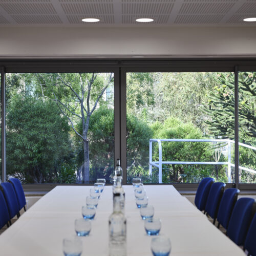TV Meeting Room set up in boardroom style with glasses and water and a view of the Darwin Garden at Christ's College, Cambridge.