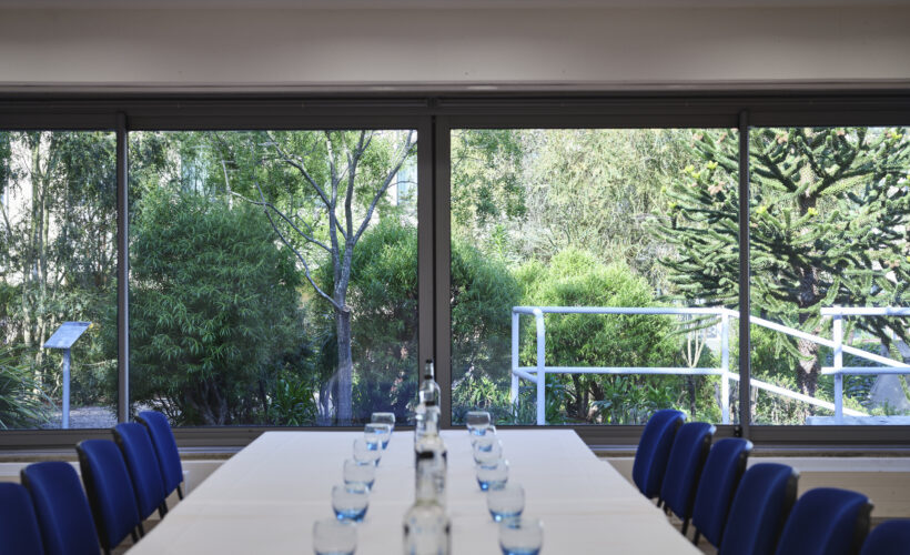 TV Meeting Room set up in boardroom style with glasses and water and a view of the Darwin Garden at Christ's College, Cambridge.