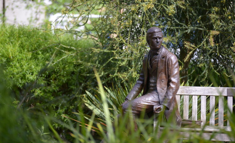 Darwin Garden at Christ’s College, Cambridge, with a bronze statue of Charles Darwin seated among landscaped planting and trees in a quiet courtyard