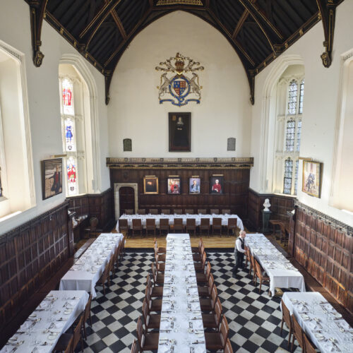 An aerial shot of the Great Hall featuring beautiful stained glass ornate windows and the tables set up with white table clothes for a special function.