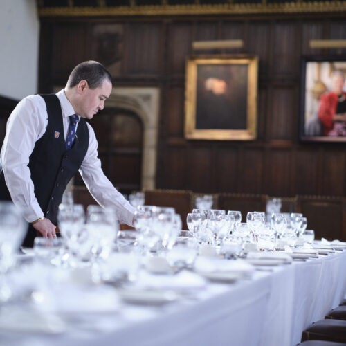 Great Hall at Christ's College being set up for dinner with portraits of key connections in the background. Our events often receive great client reviews.